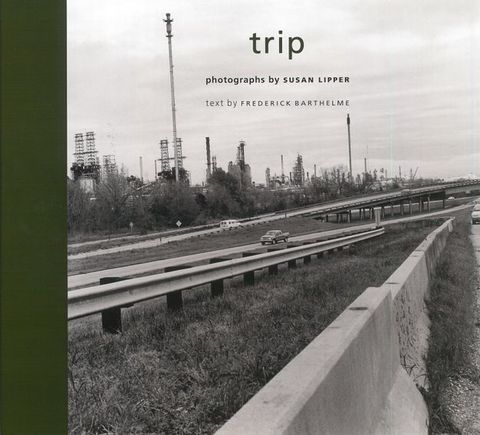 Book cover. Black and white photograph shows roads and a jersey wall zooming away from us from the lower left corner into the distance to our right.