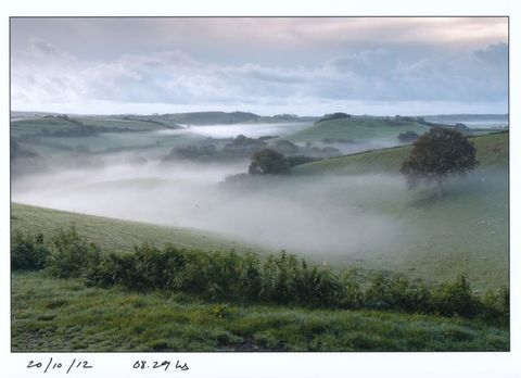 Thick, seemingly tangible fog pools in valleys that meander back through rolling hills in this landscape. Handwritten text under the photograph provides the date and time.