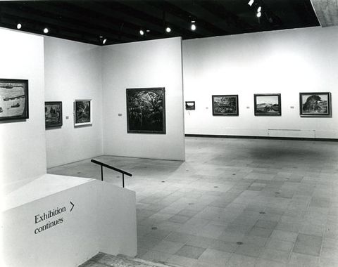 Installation. Black and white photograph shows eight paintings hung widely spaced along white walls.